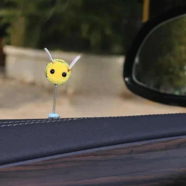 Small yellow and black fur ball bee car decoration on a plastic surface.