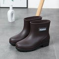Women's black PVC mid-calf rain boot with a low heel on a wet surface.