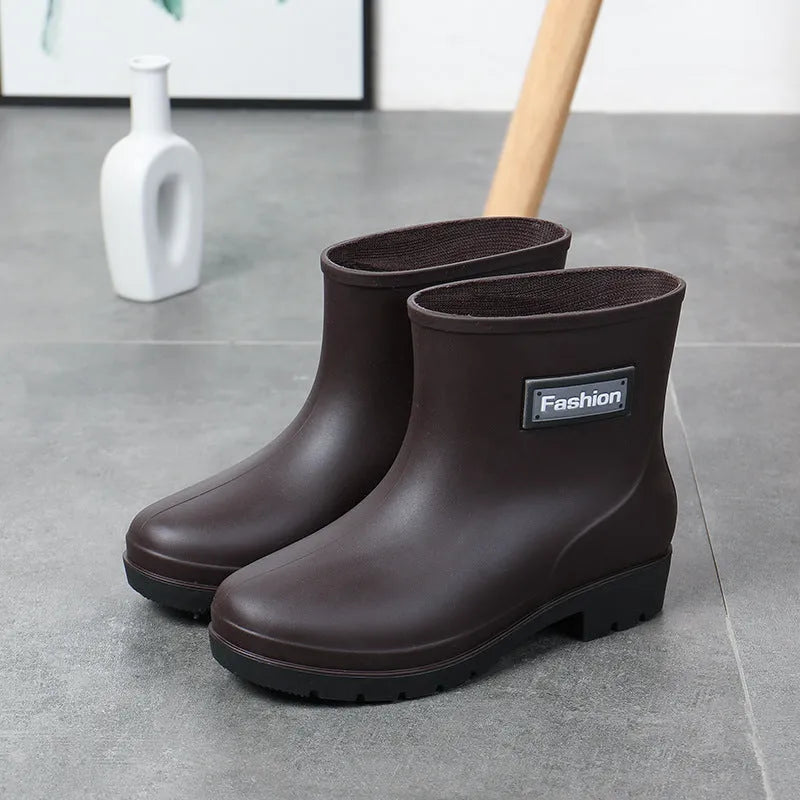 Women's black PVC mid-calf rain boot with a low heel on a wet surface.