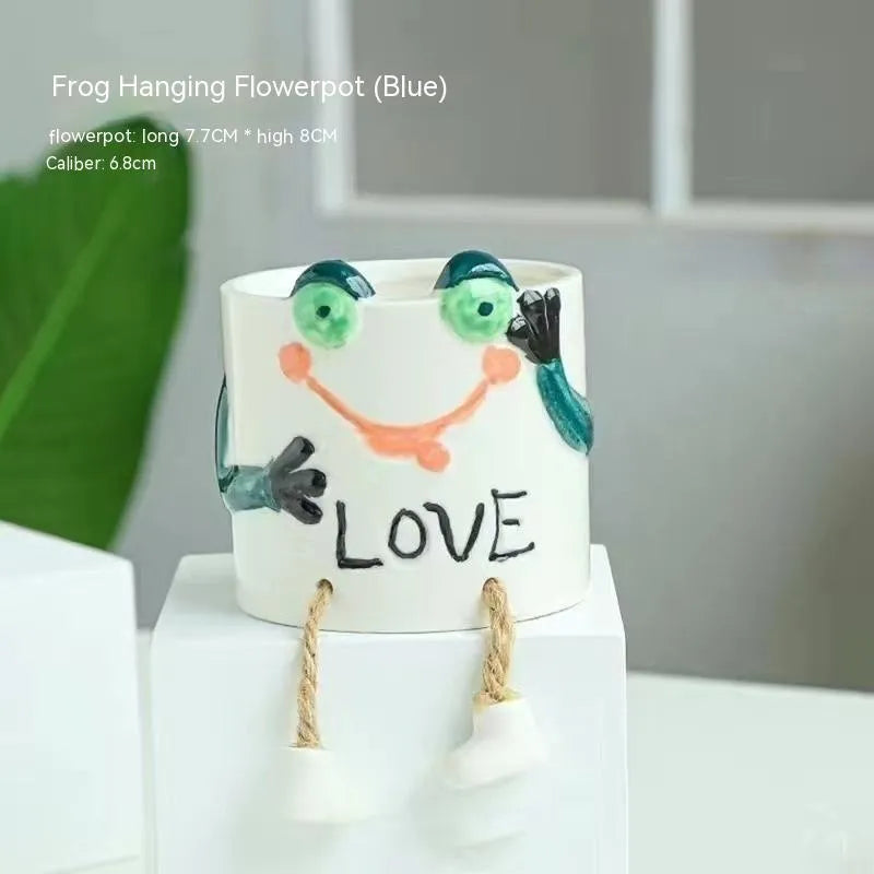 Ceramic hanging foot flowerpot in a cartoon style, shown on a desktop with a small succulent plant.