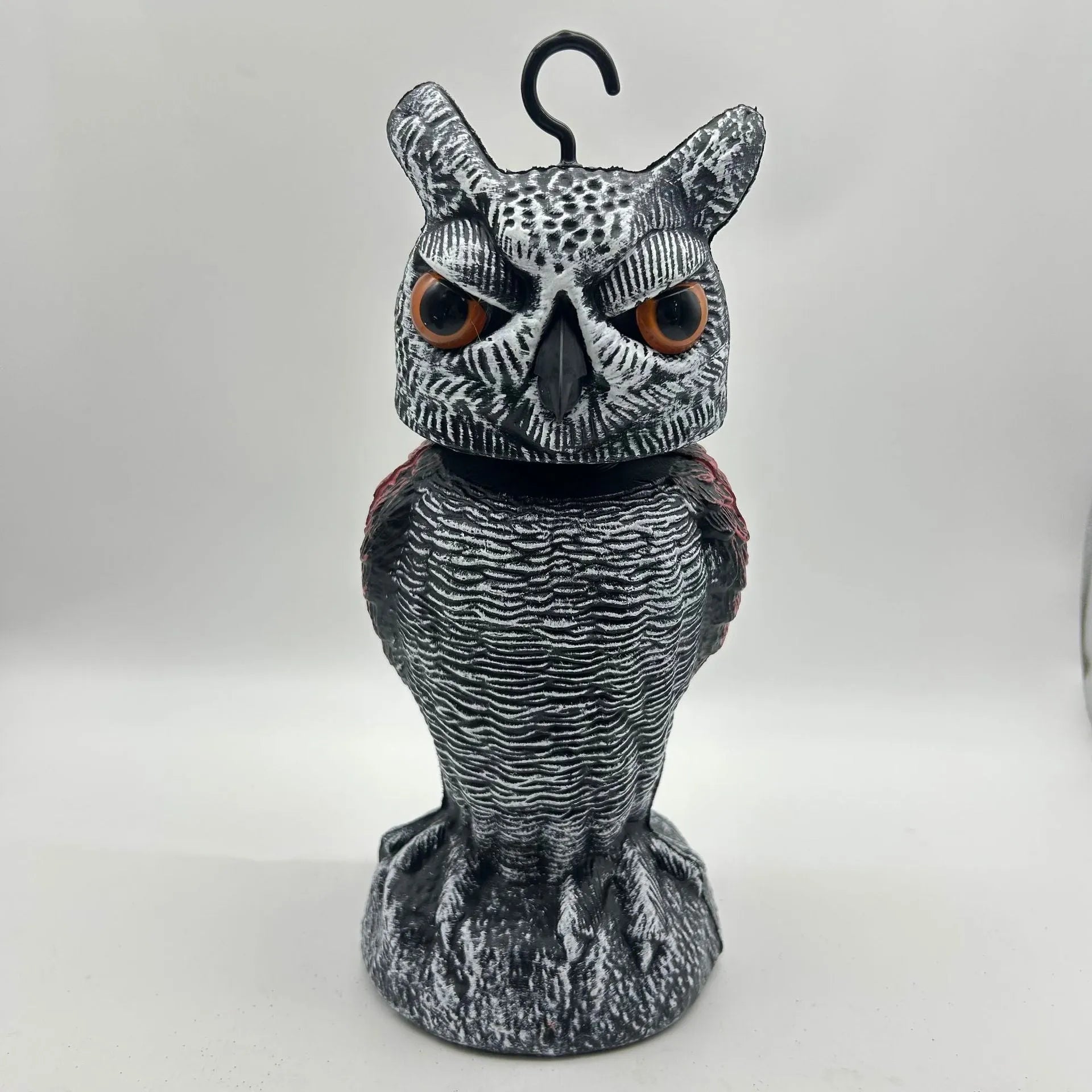 A detailed artificial owl bird scare ornament with a shaking head, shown in a garden setting.