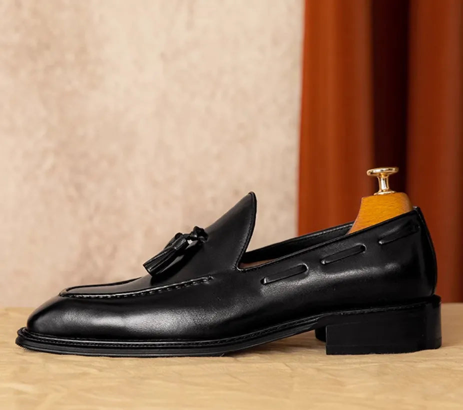 Men's black leather slip-on loafers with a fringed detail on the vamp and a rubber sole.