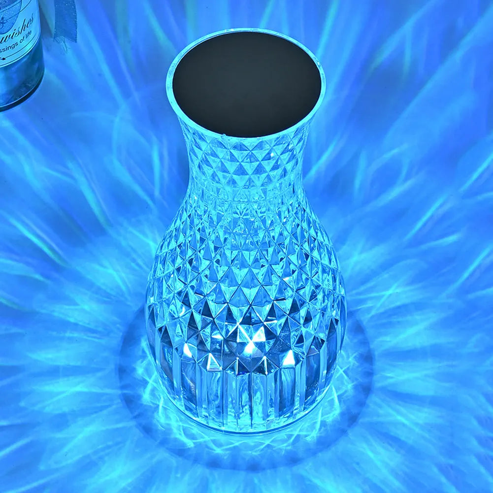 Transparent vase-shaped crystal LED table lamp on a table, showing soft coloured light.