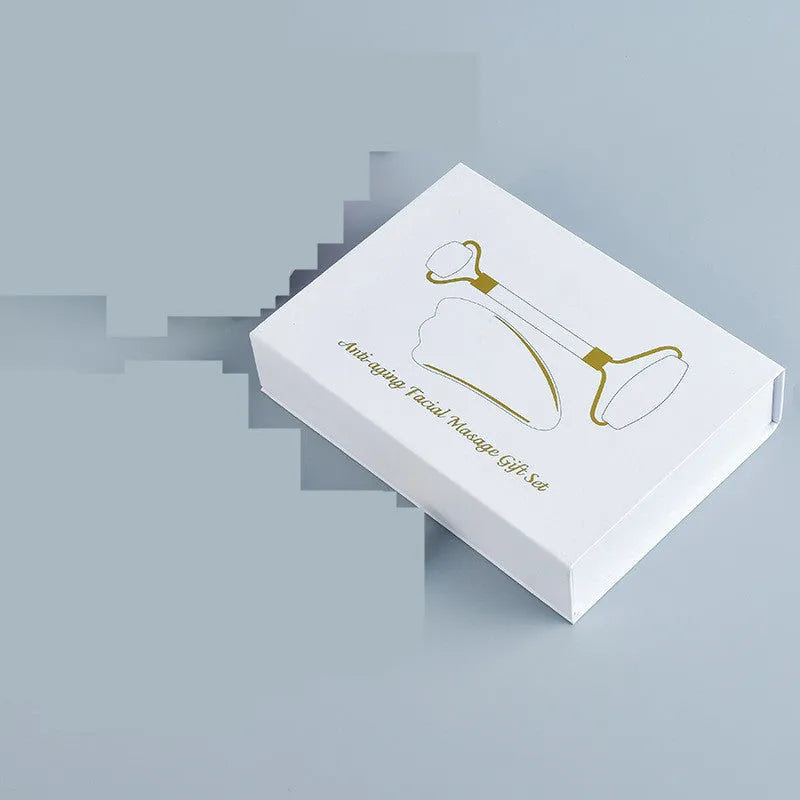White jade double-headed facial roller and gua sha board set on a flat surface.