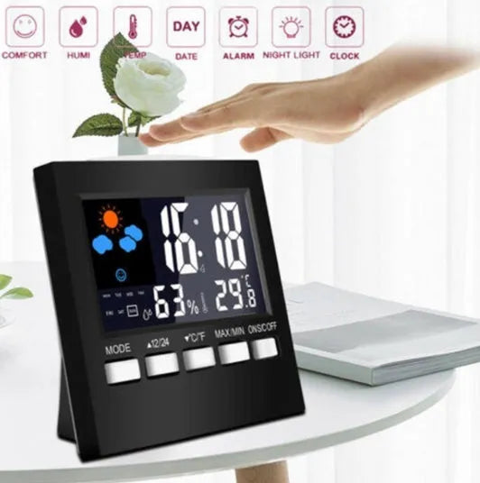 Black digital alarm clock thermometer displaying temperature and time on a desk