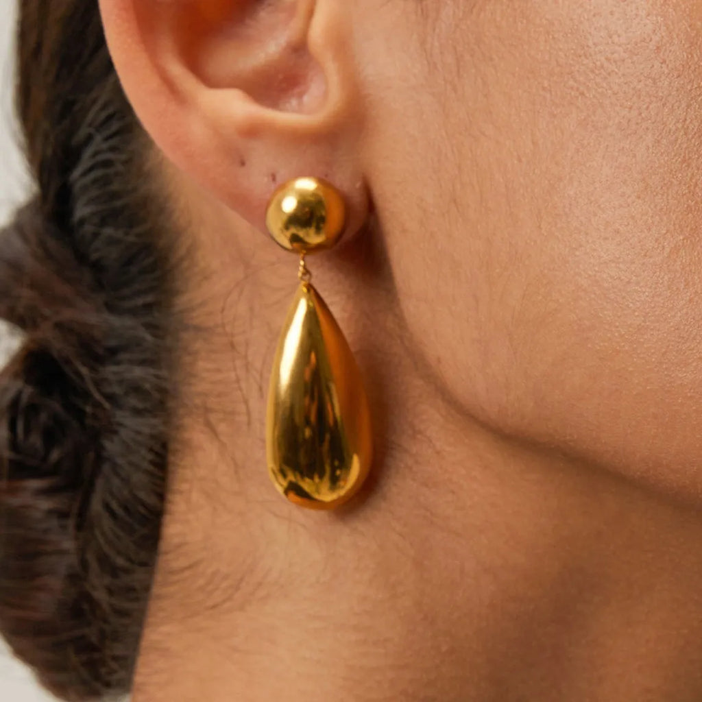 A pair of gold-coloured geometric earrings with a hemisphere base and dangling water drop pendant.