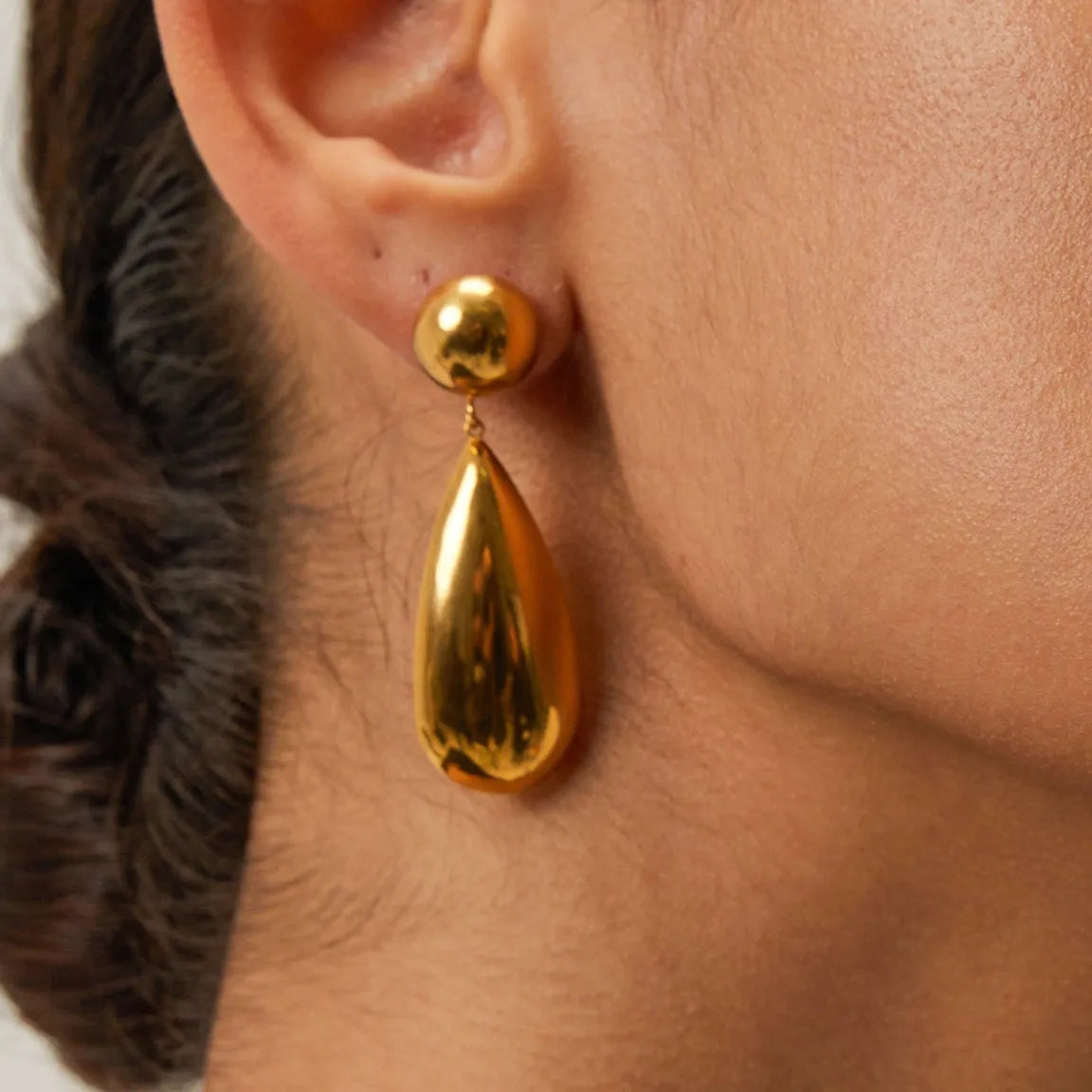 A pair of gold-coloured geometric earrings with a hemisphere base and dangling water drop pendant.