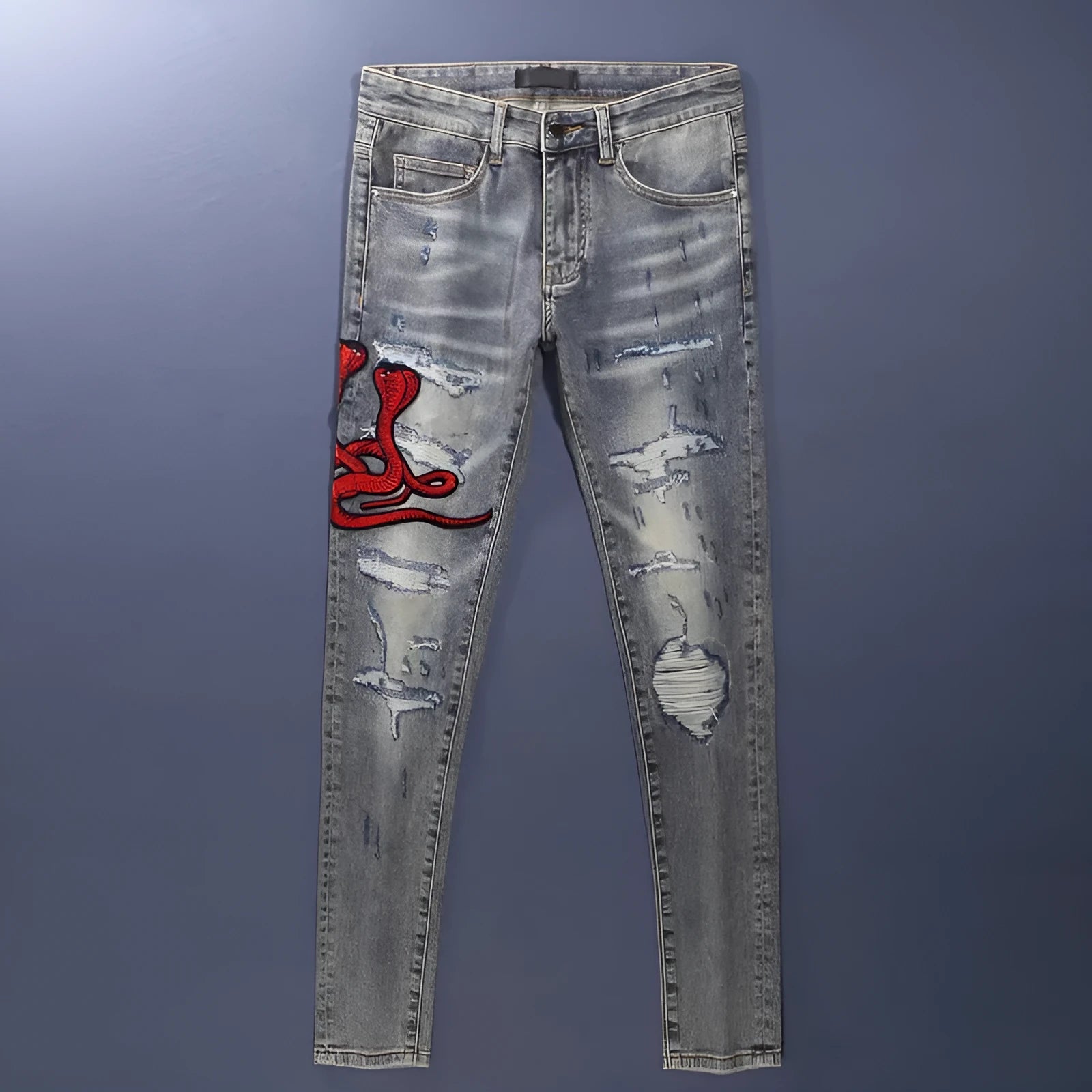 Slim-fit light blue jeans with a worn wash, knee holes, patch details, and embroidered branding on the leg.