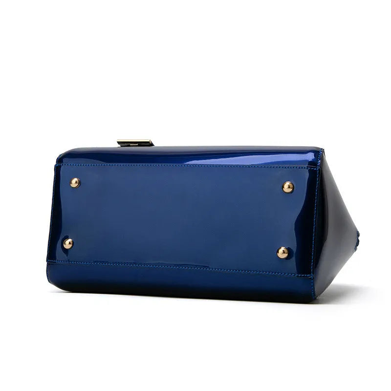 Shiny blue PVC patent leather handbag with lock closure and crossbody strap on a white background