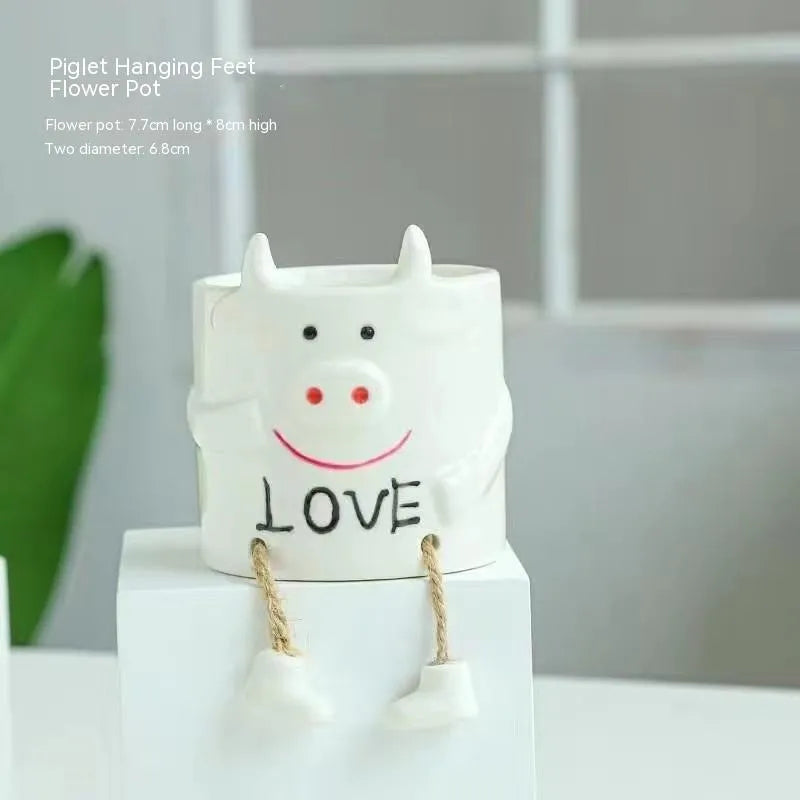 Ceramic hanging foot flowerpot in a cartoon style, shown on a desktop with a small succulent plant.