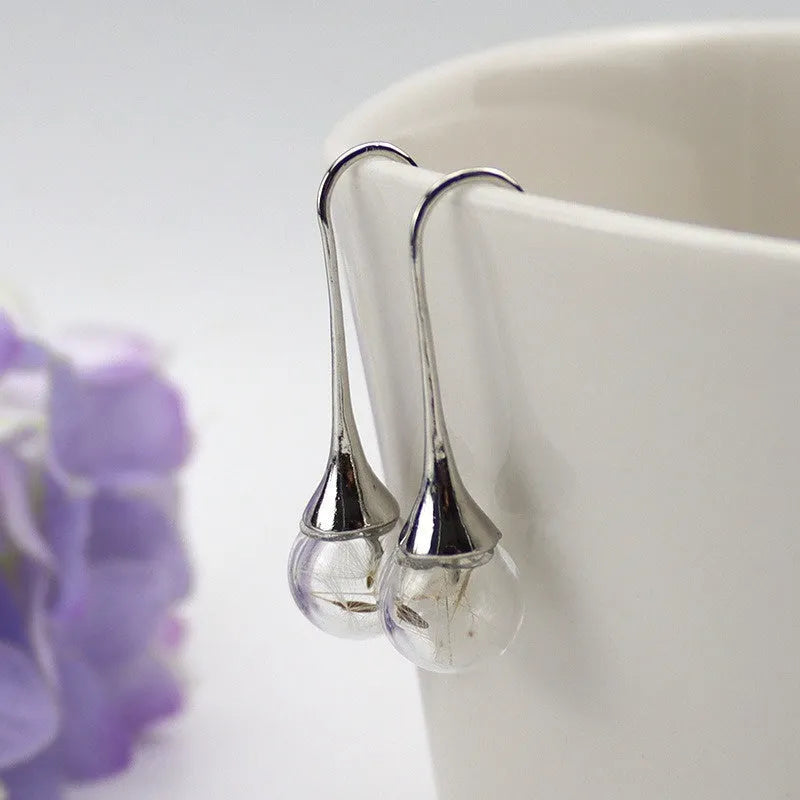 Close-up of transparent glass dandelion seed earrings on a French hook in silver finish.