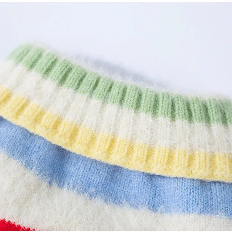 Corgi dog wearing a rainbow apple striped knitted pullover sweater in brown, standing on grass