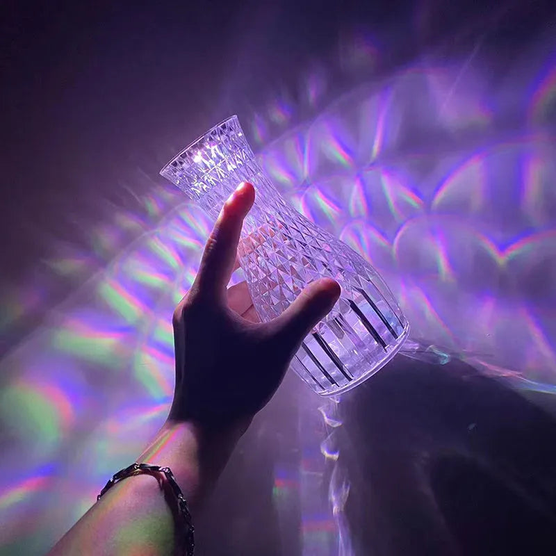 Transparent vase-shaped crystal LED table lamp on a table, showing soft coloured light.
