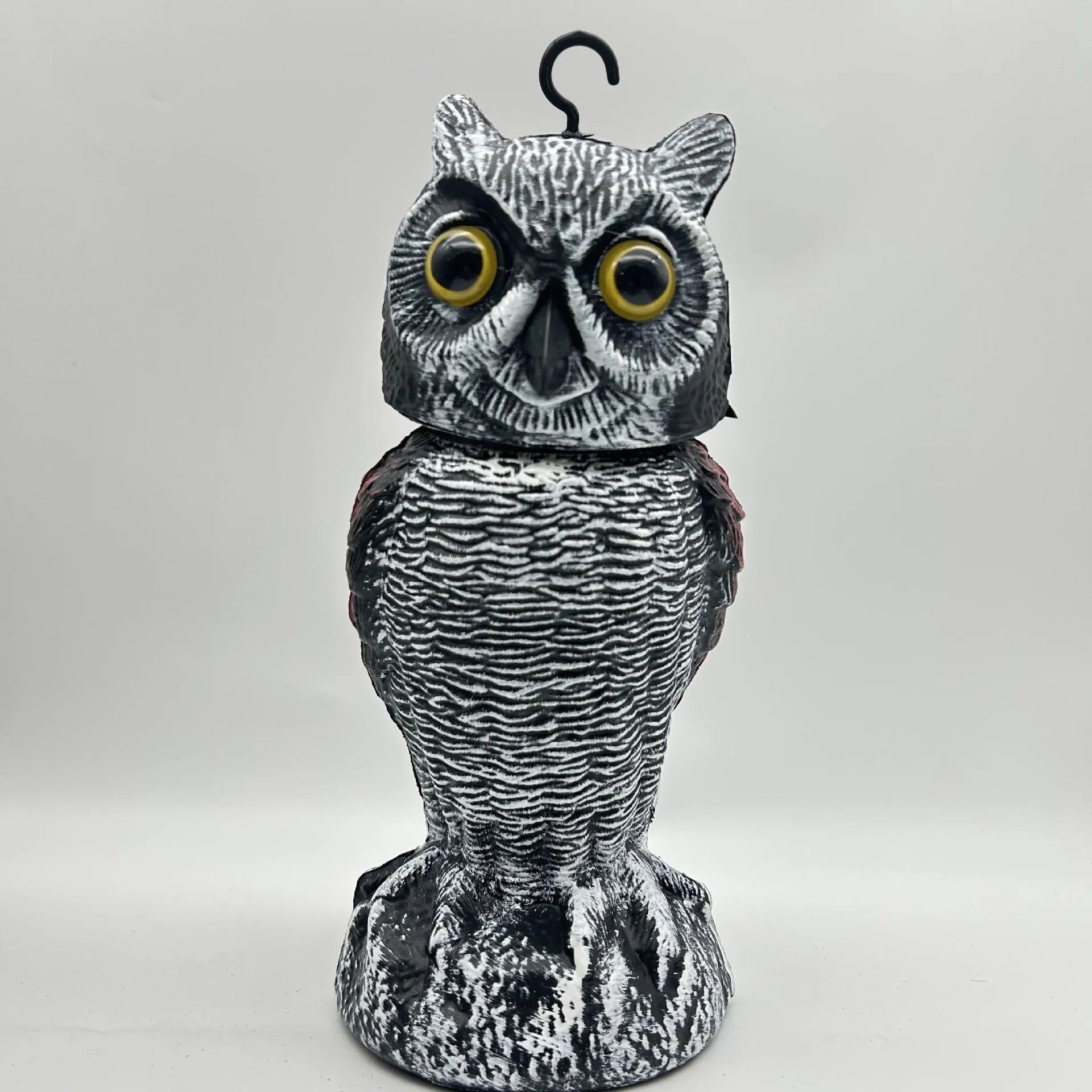 A detailed artificial owl bird scare ornament with a shaking head, shown in a garden setting.