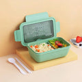 Green partitioned bento lunch box with four food compartments, shown open.