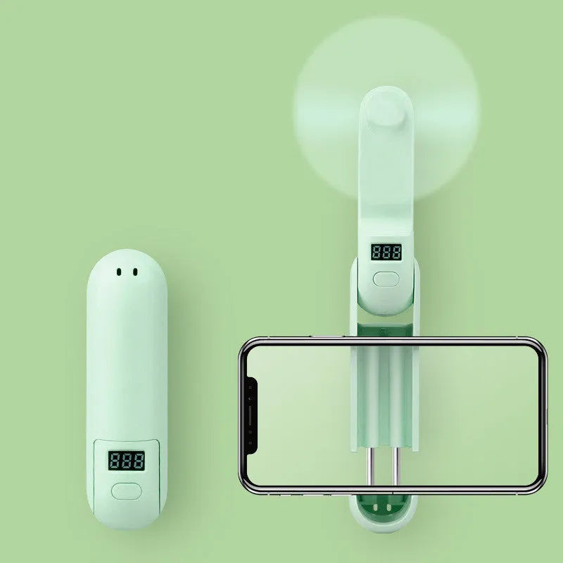 Green folding mini fan with plastic blades collapsed for storage beside USB charging cable