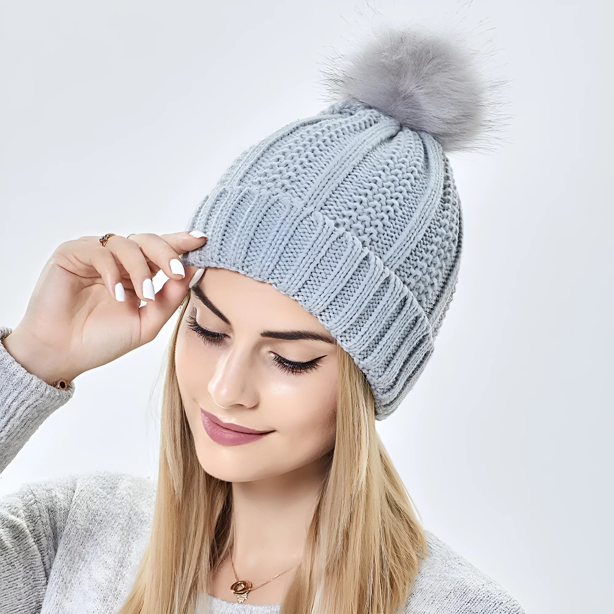 Women's beige wool knit beanie hat with a faux fur pom pom and a satin lining visible at the brim.