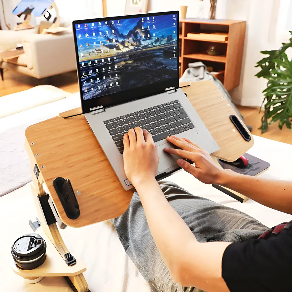 Wooden folding computer desk on a bed showing adjustable angle and laptop.