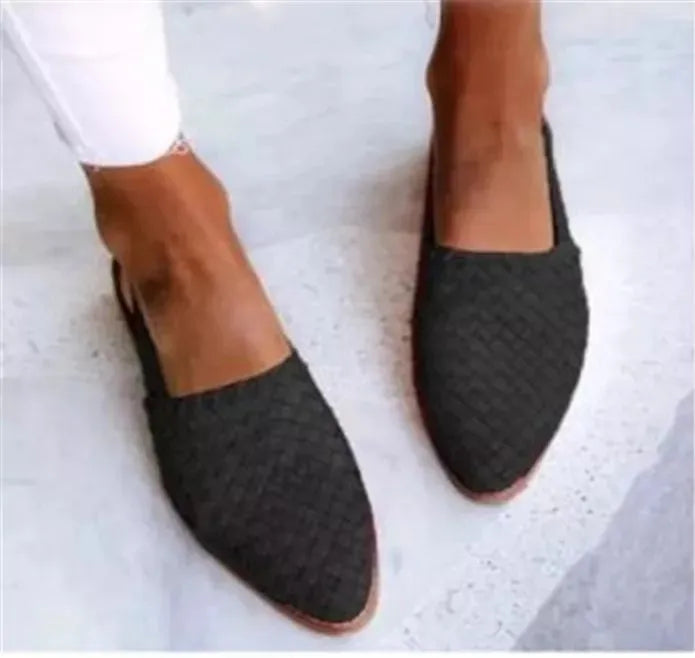 A pair of black baotou flat sandals with a buckle fastening and pointed toe on a plain background.