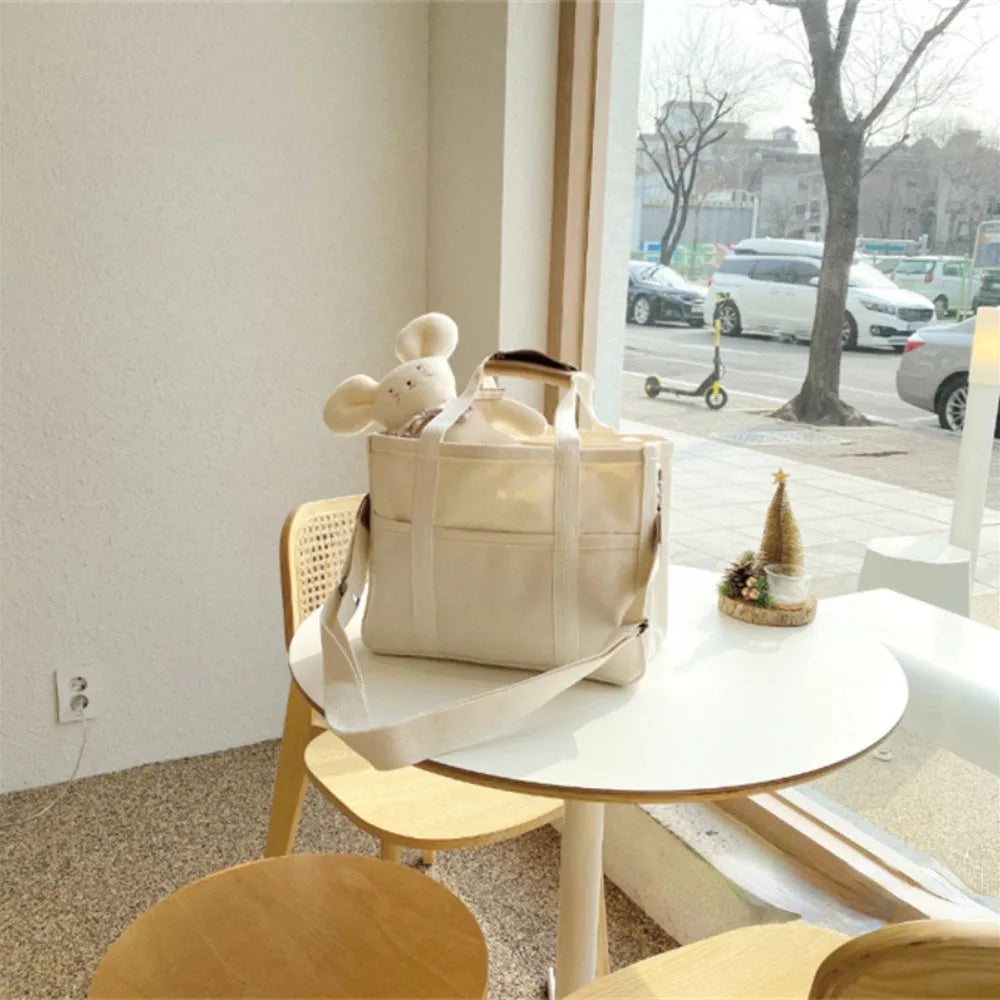 Beige canvas crossbody mommy bag holding baby bottles and wipes on table