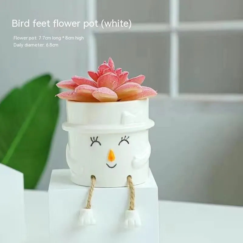 Ceramic hanging foot flowerpot in a cartoon style, shown on a desktop with a small succulent plant.