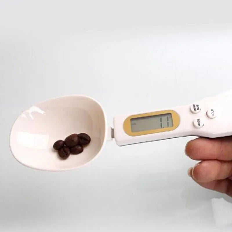 White digital kitchen spoon scale with LCD display showing 0.0g on a wooden table