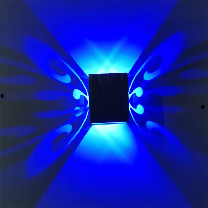 Modern aluminium butterfly-shaped LED wall lamp on a white wall with remote control.