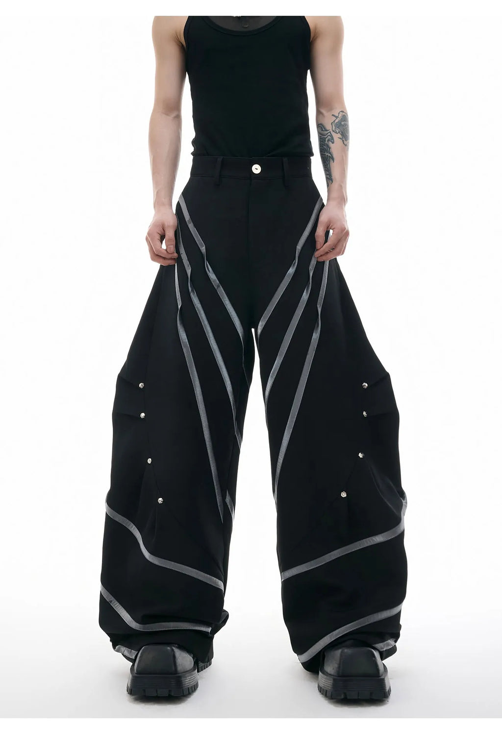 Men's black trousers with a deconstructing three-dimensional cut and pleats secured with metal striped rivets.
