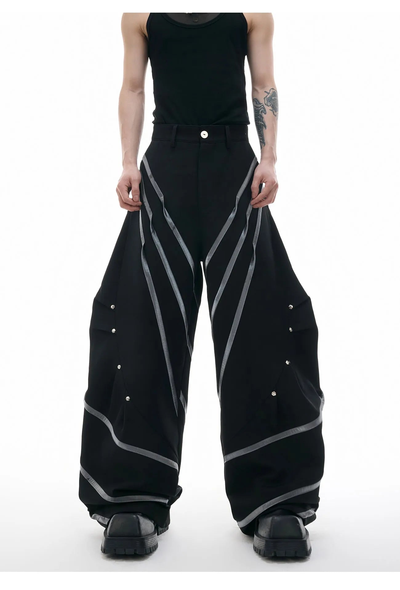 Men's black trousers with a deconstructing three-dimensional cut and pleats secured with metal striped rivets.