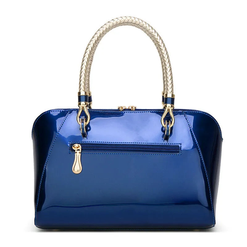 Shiny blue PVC patent leather handbag with lock closure and crossbody strap on a white background