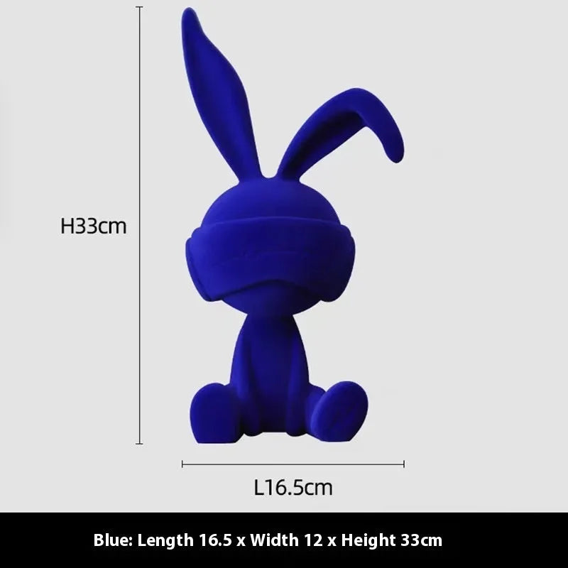 Green resin rabbit table ornament with a suede blindfold on a wooden shelf.
