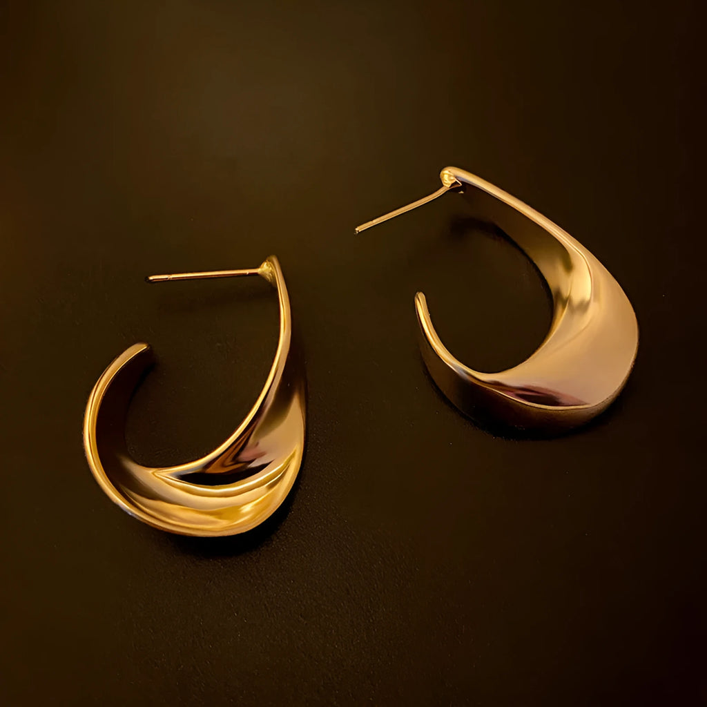 A pair of twisted geometric design metal earrings in a gold colour on a plain background