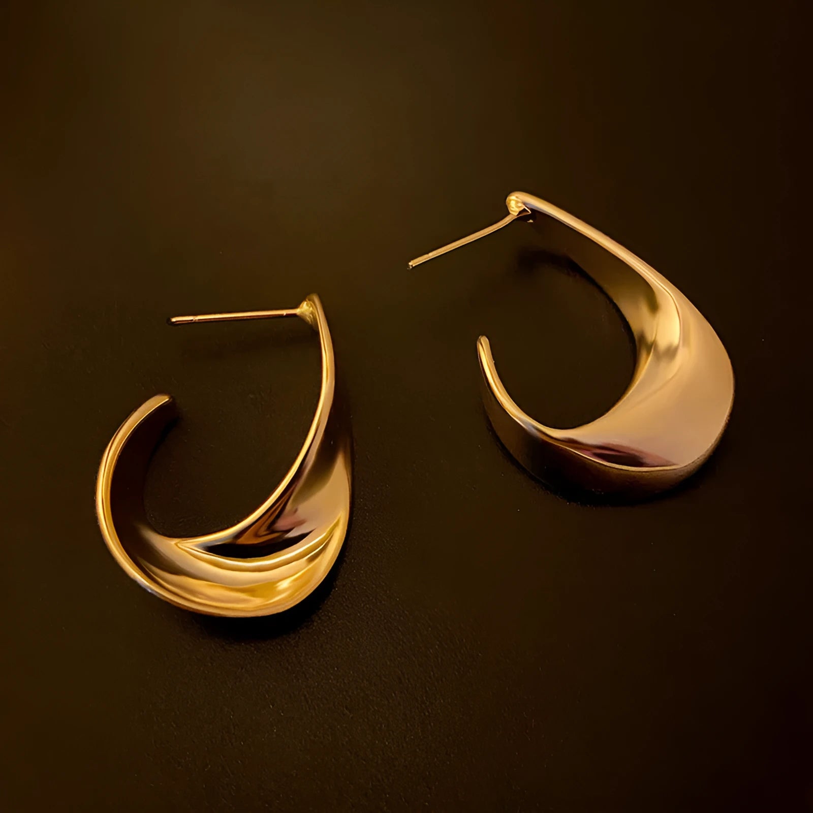 A pair of twisted geometric design metal earrings in a gold colour on a plain background