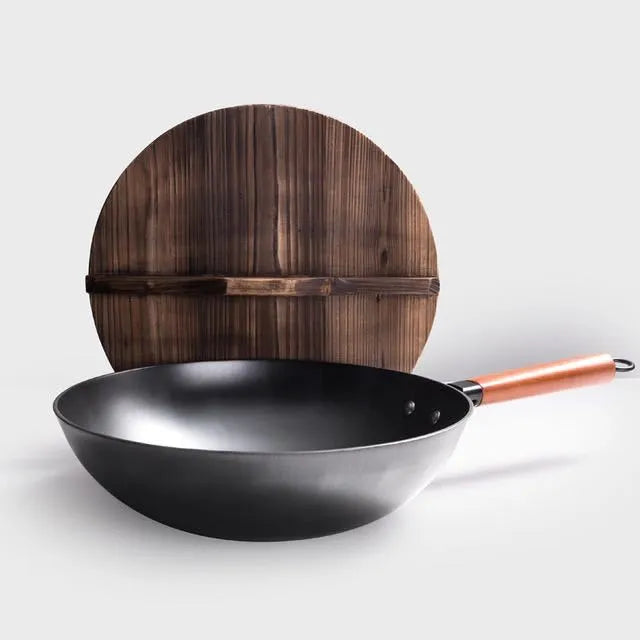 Black handmade traditional iron wok with a wooden handle on a stovetop.