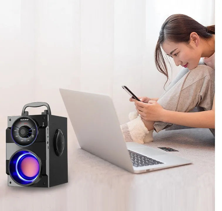 Black portable mini home audio system with subwoofer, satellite speakers, and USB charging cable on a desk.