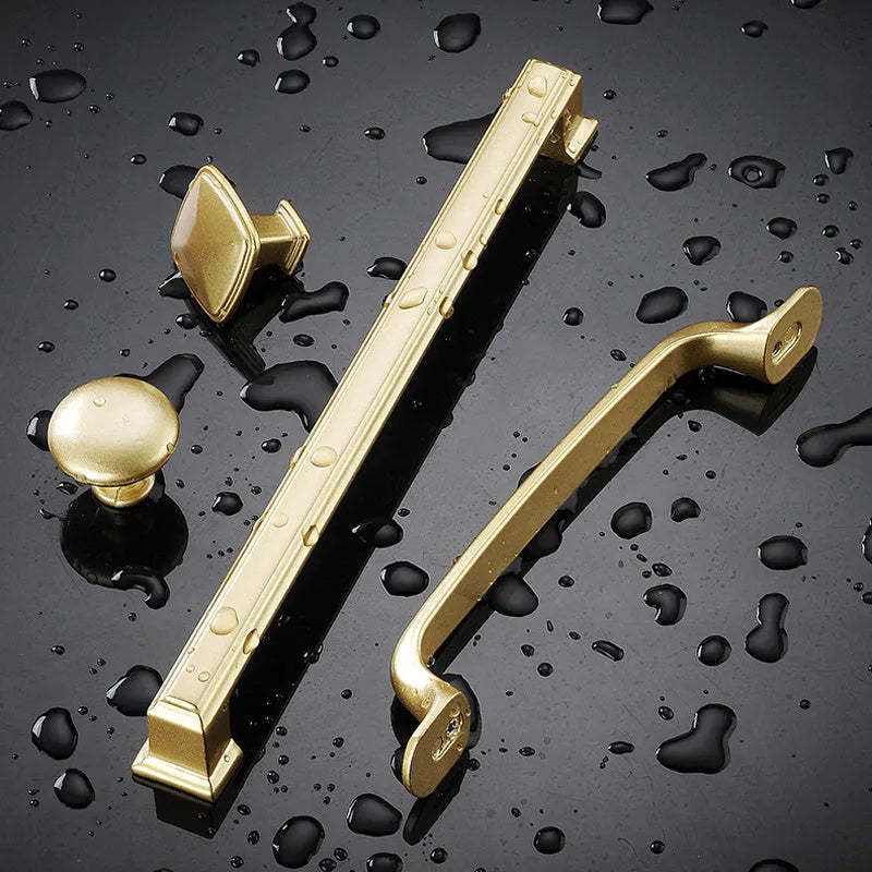 Gold coloured T-shaped aluminium alloy single hole cabinet door handle on a white background.