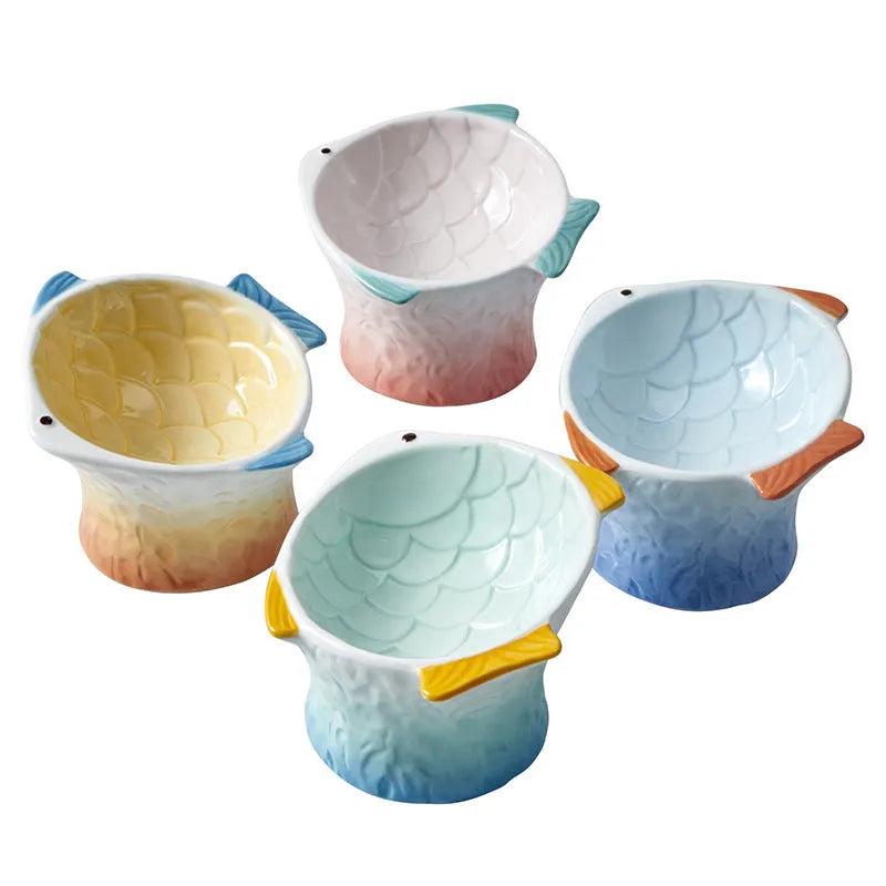 Blue fish-shaped ceramic cat bowl with tilted design and non-slip base on a wooden surface.