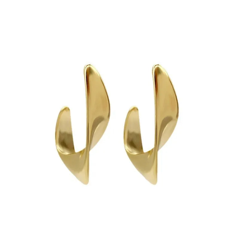 A pair of twisted geometric design metal earrings in a gold colour on a plain background