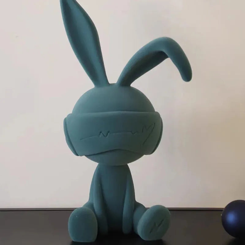 Green resin rabbit table ornament with a suede blindfold on a wooden shelf.