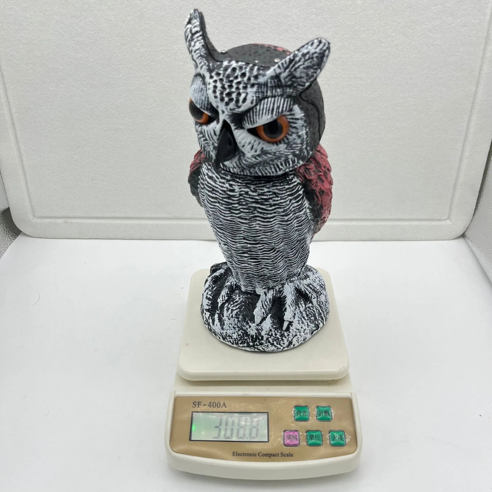 A detailed artificial owl bird scare ornament with a shaking head, shown in a garden setting.