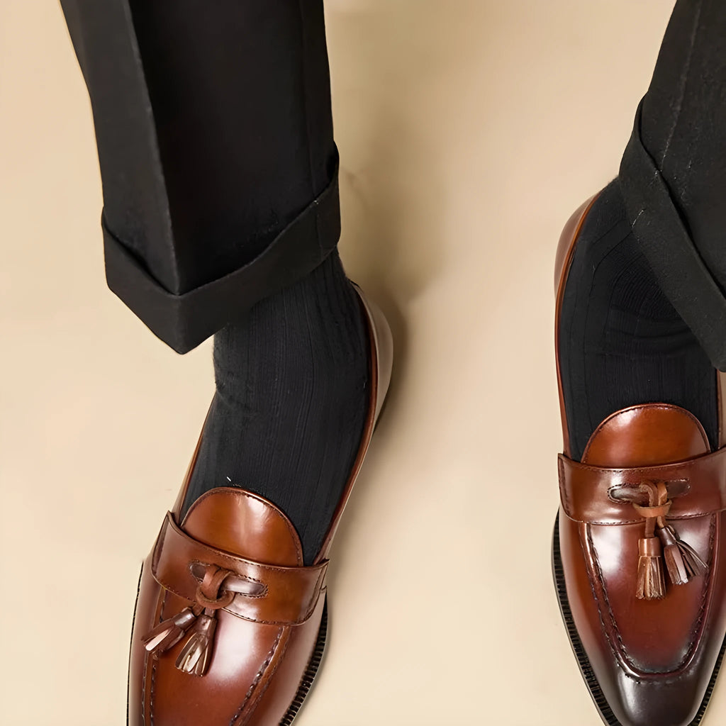 Men's black genuine leather tassel loafers on a solid background, showing polished upper and rubber sole.