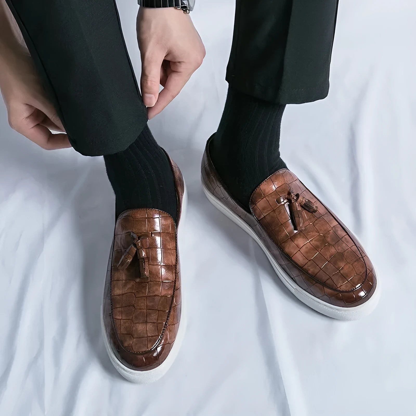 Men's black tassel detail slip-on sneakers with a round toe and rubber sole on a white background.