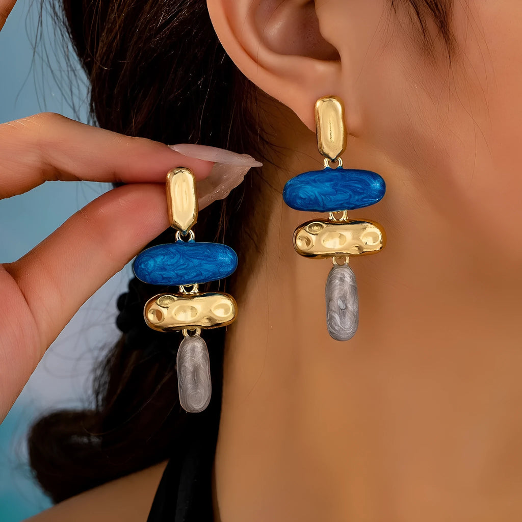 A pair of geometric-shaped stud earrings with a multicolour metallic finish on a plain background.