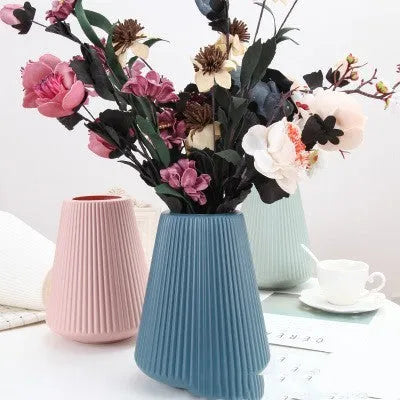 A simple white melamine plastic decorative flower vase on a wooden tabletop.