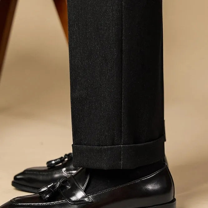Men's black genuine leather tassel loafers on a solid background, showing polished upper and rubber sole.