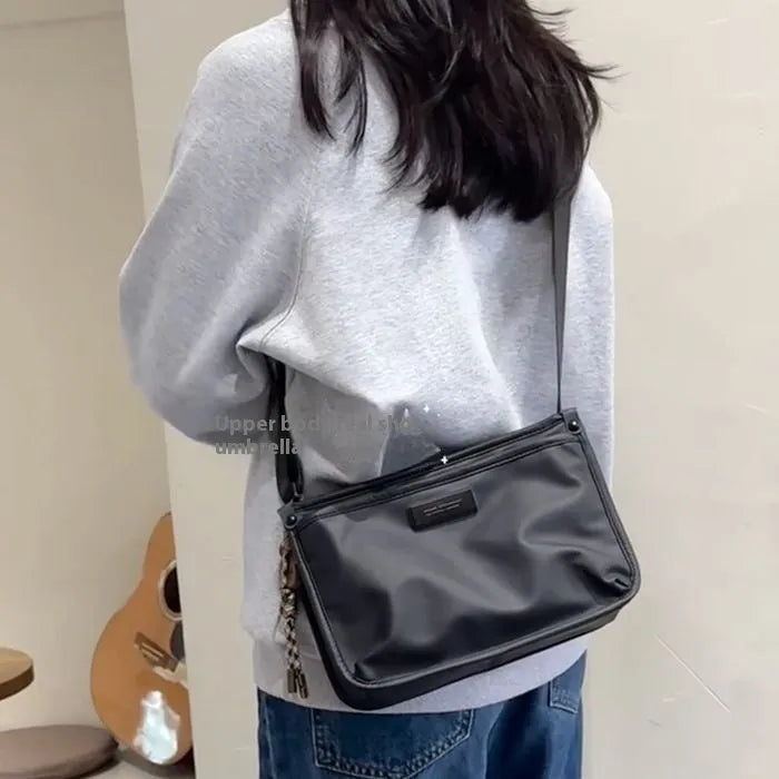 A small square crossbody bag in a cool retro style, made from textured Oxford cloth, shown on a person for scale.