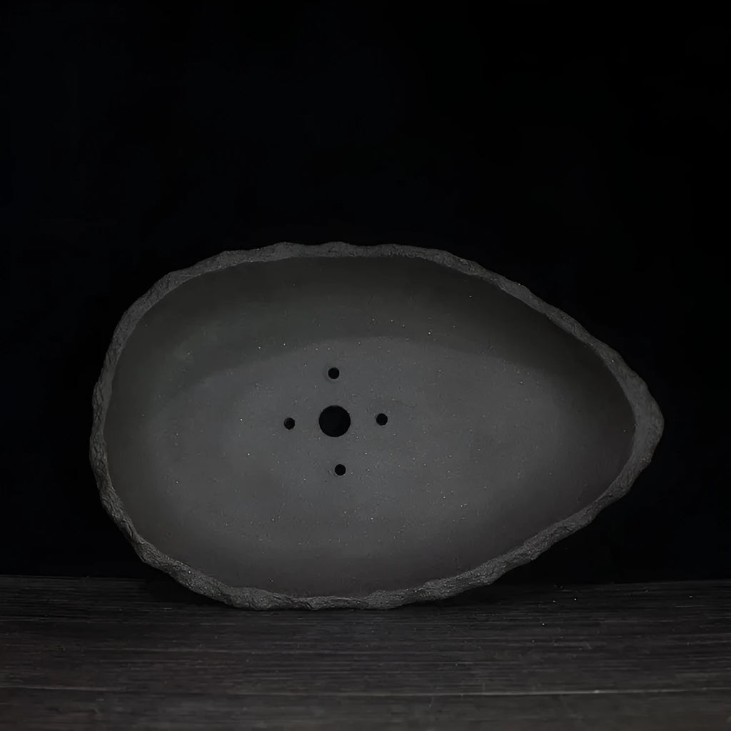 Handmade purple clay flower pot with creative shape on floor next to plant.