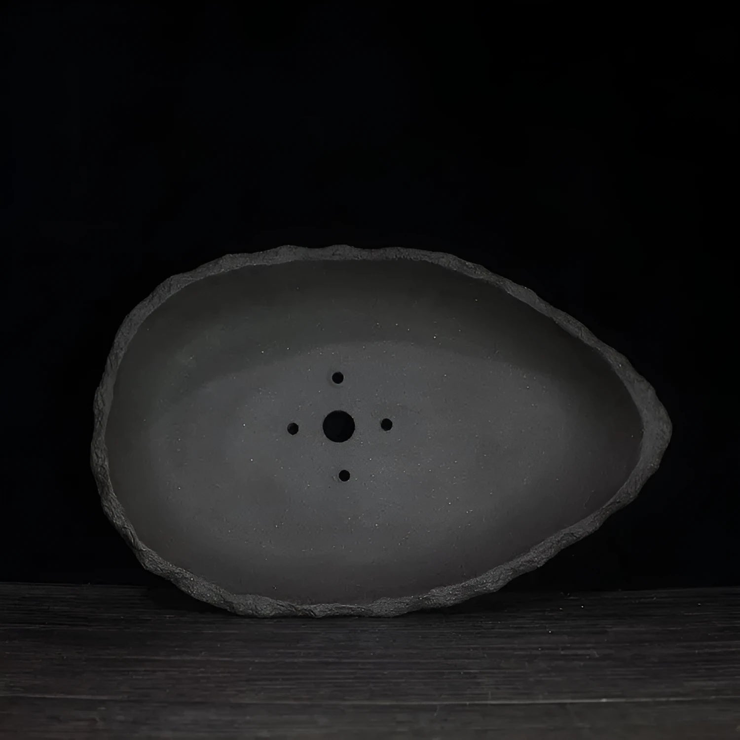 Handmade purple clay flower pot with creative shape on floor next to plant.