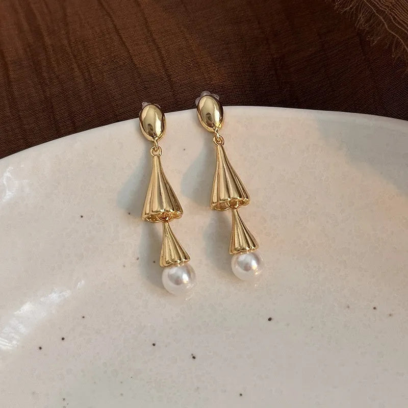 Gold electroplated copper geometric fringe earrings on a woman with long wind chime pearl mosquito coil plate shape close up
