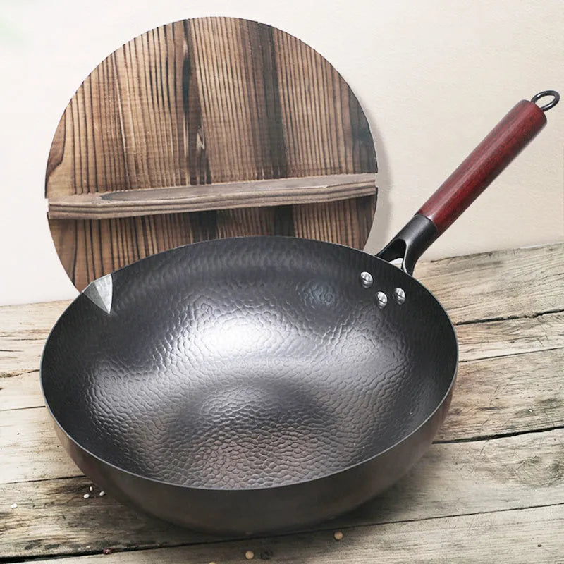 Black handmade traditional iron wok with a wooden handle on a stovetop.